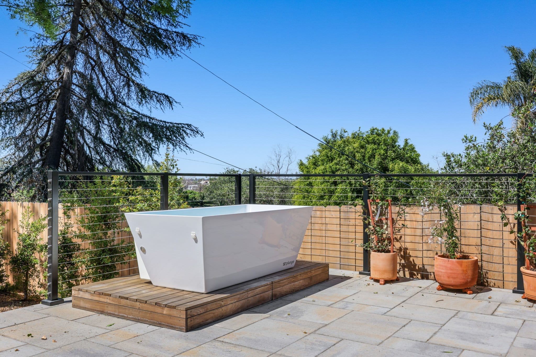 outdoor deck with freestanding soaking tub on wood platform and cable railing