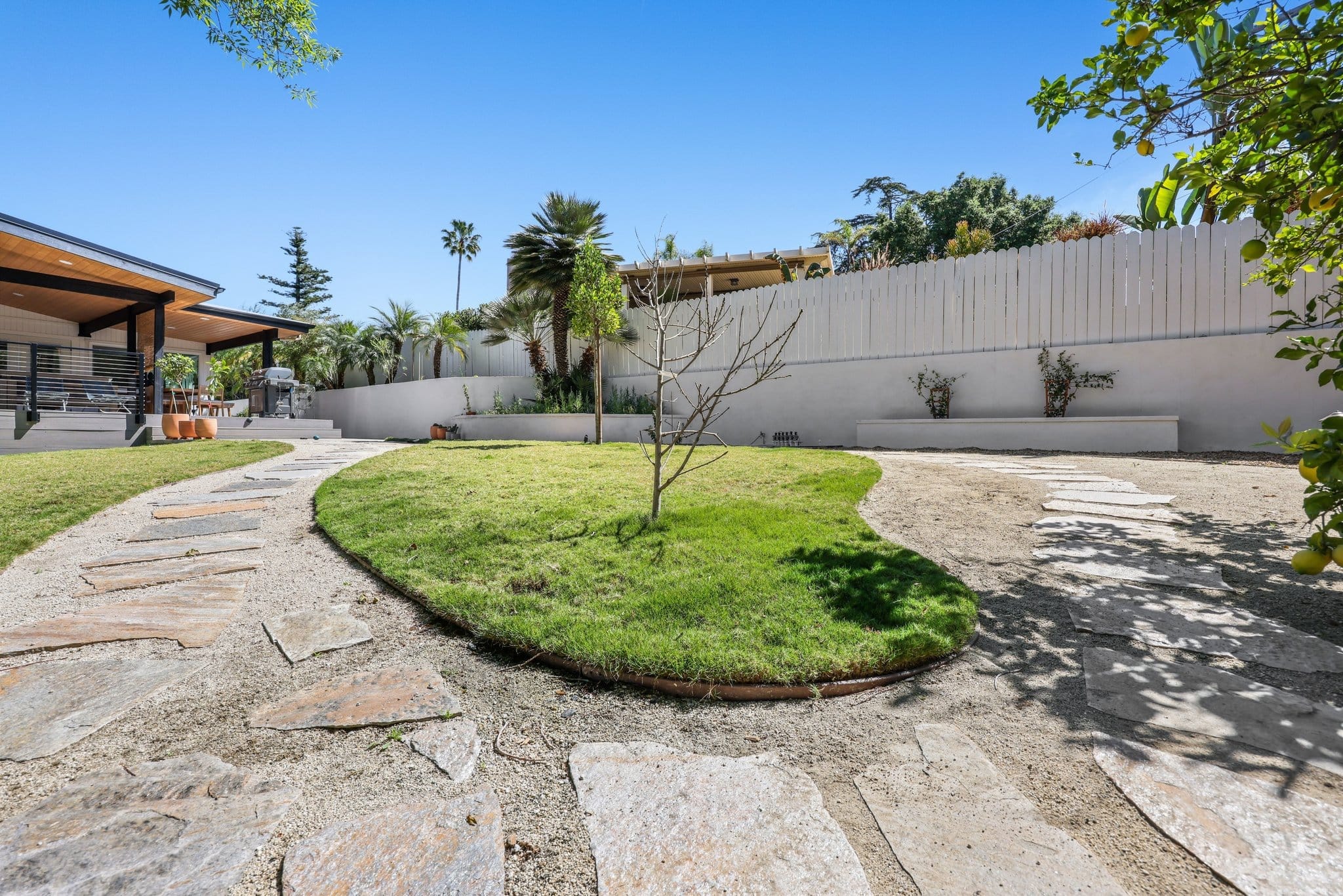 Sunny backyard with curved flagstone walkway, manicured lawn and covered patio