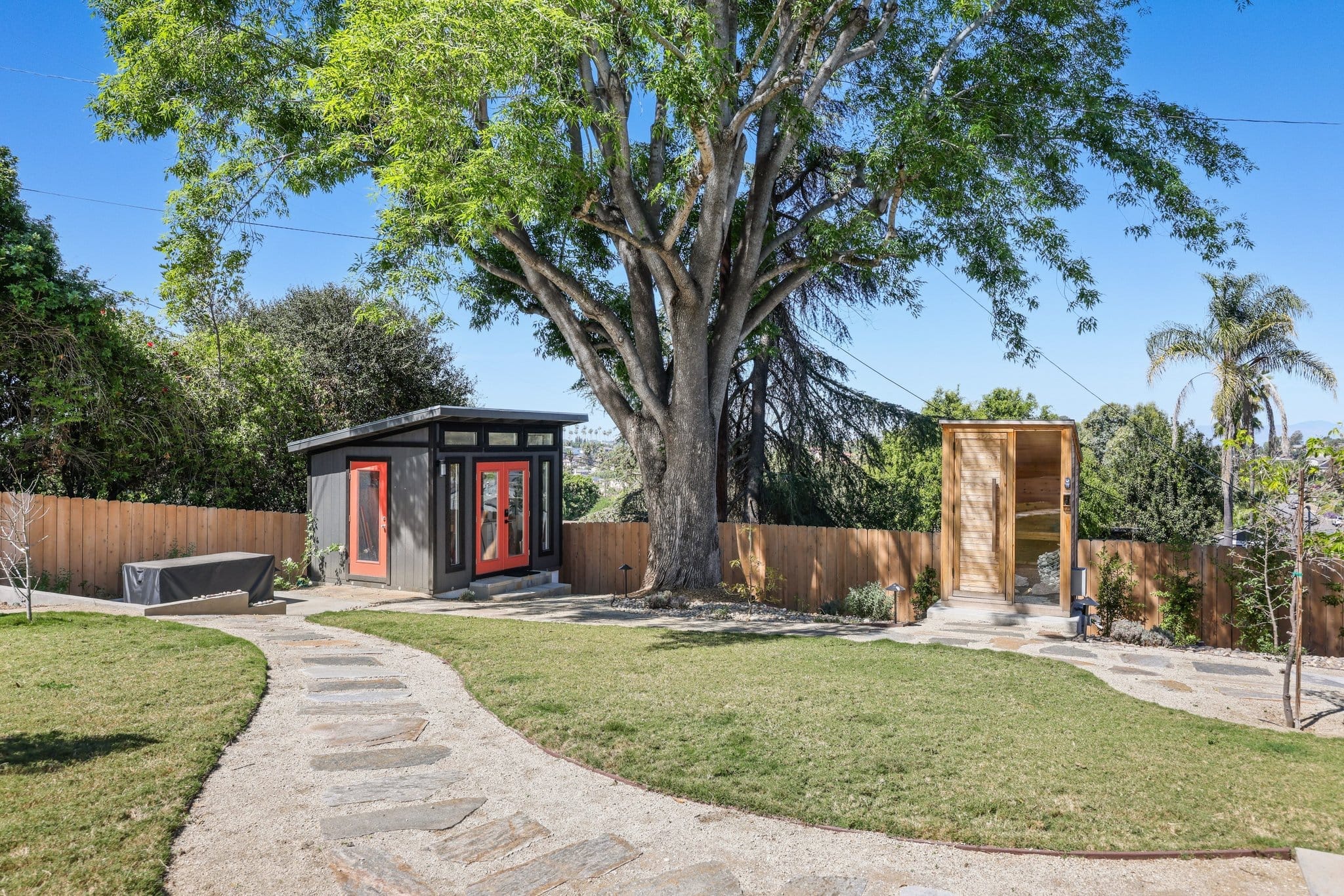 Spacious backyard featuring modern detached studio shed and cedar outdoor structure under mature tree
