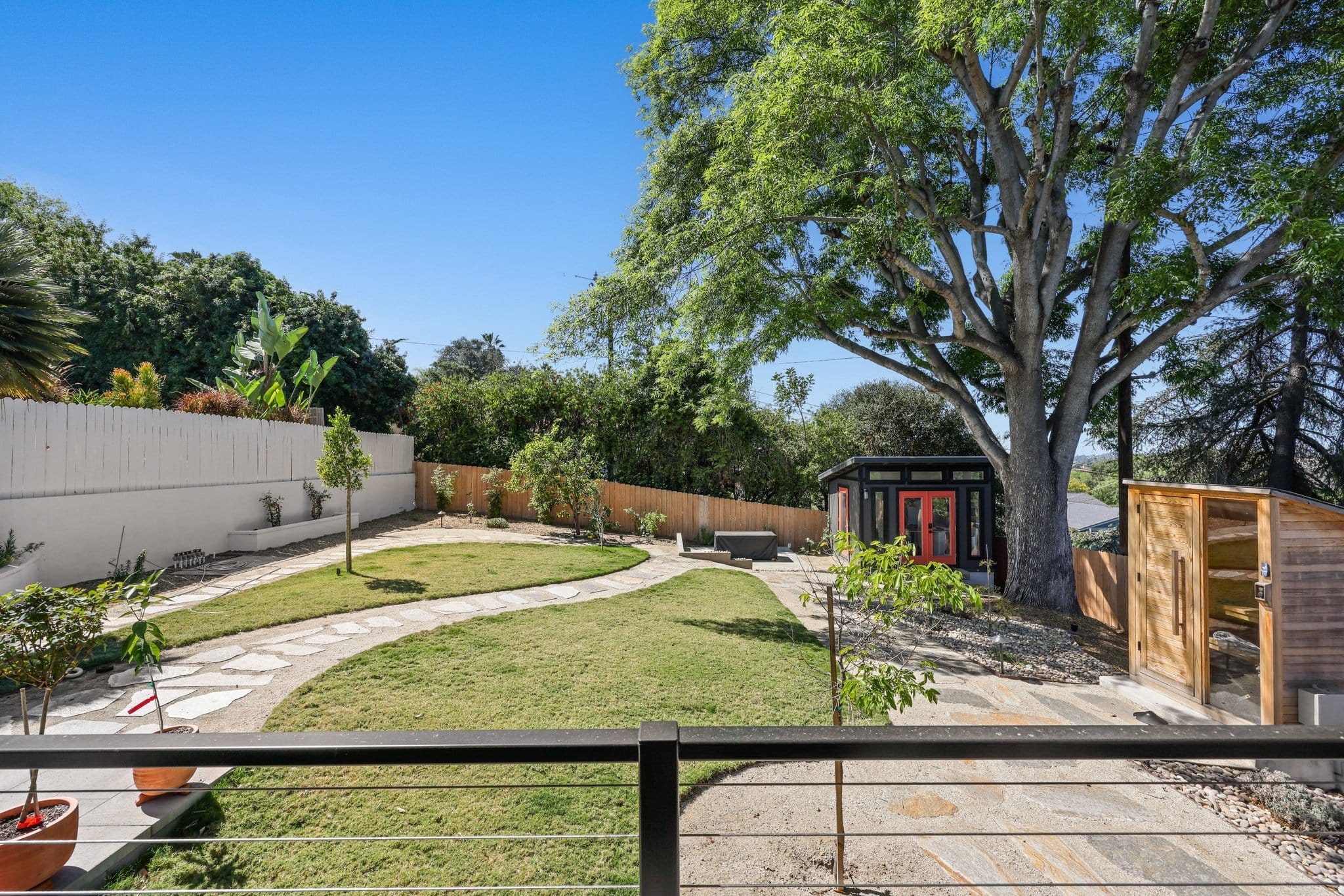 Landscaped backyard with manicured lawn, stone pathway, mature shade tree and detached studio