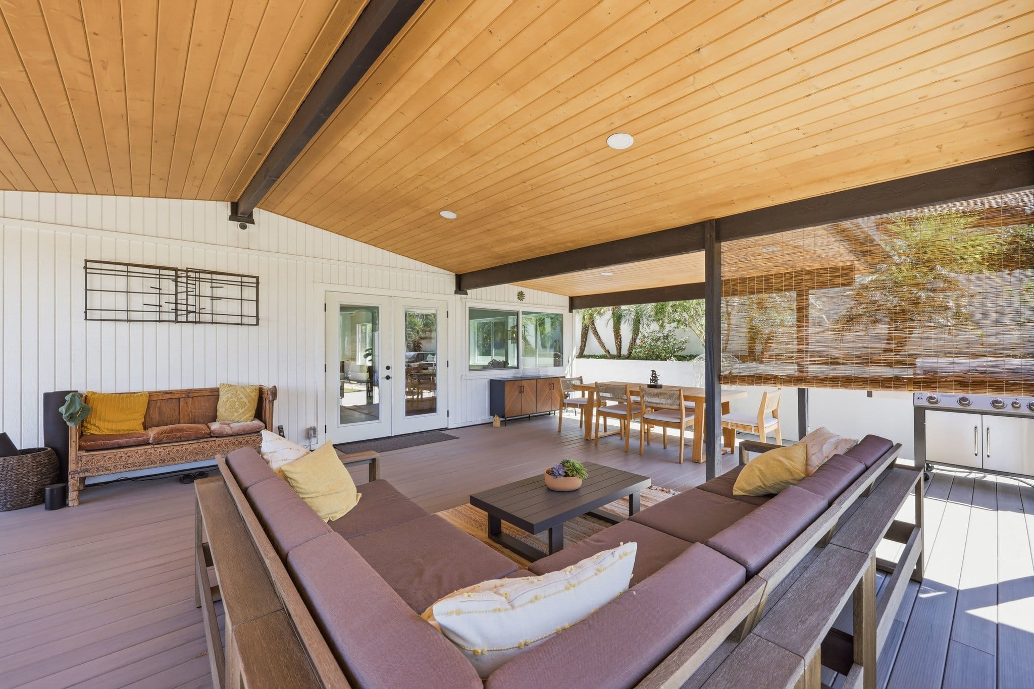 Covered deck living and dining area beneath warm wood vaulted ceiling with built-in grill