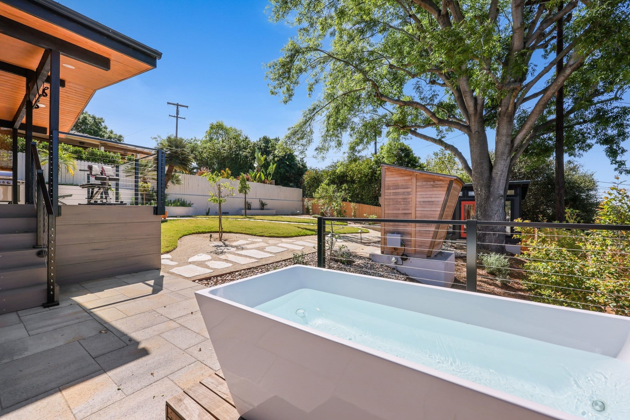 Backyard patio with freestanding soaking tub, cable railing and cedar privacy screen