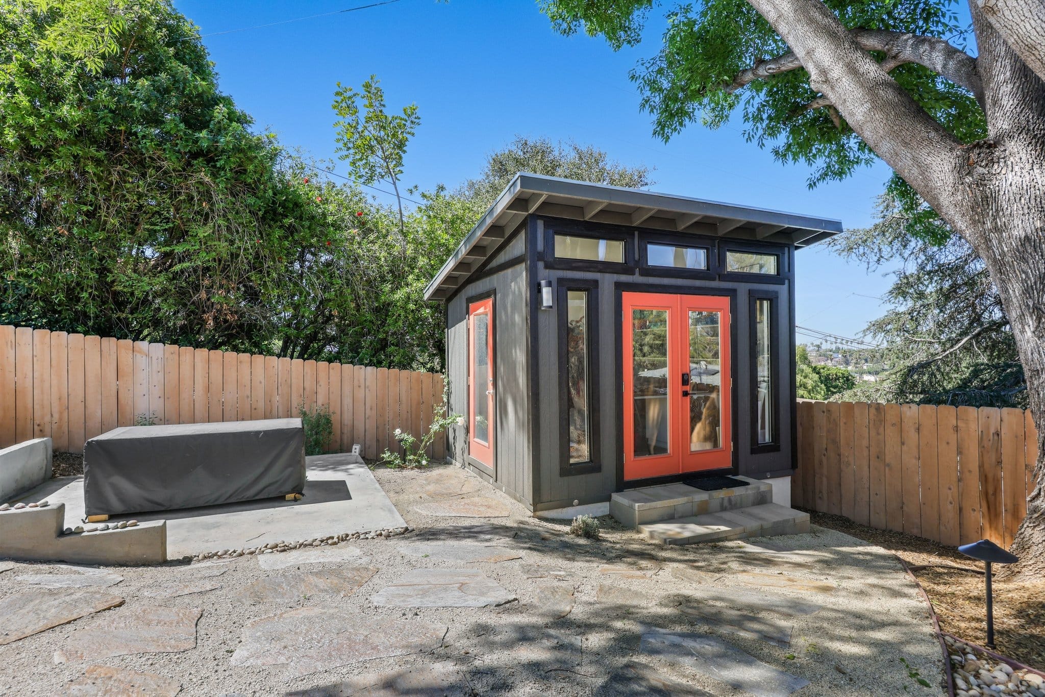 modern detached backyard studio with gray siding and orange-red glass doors