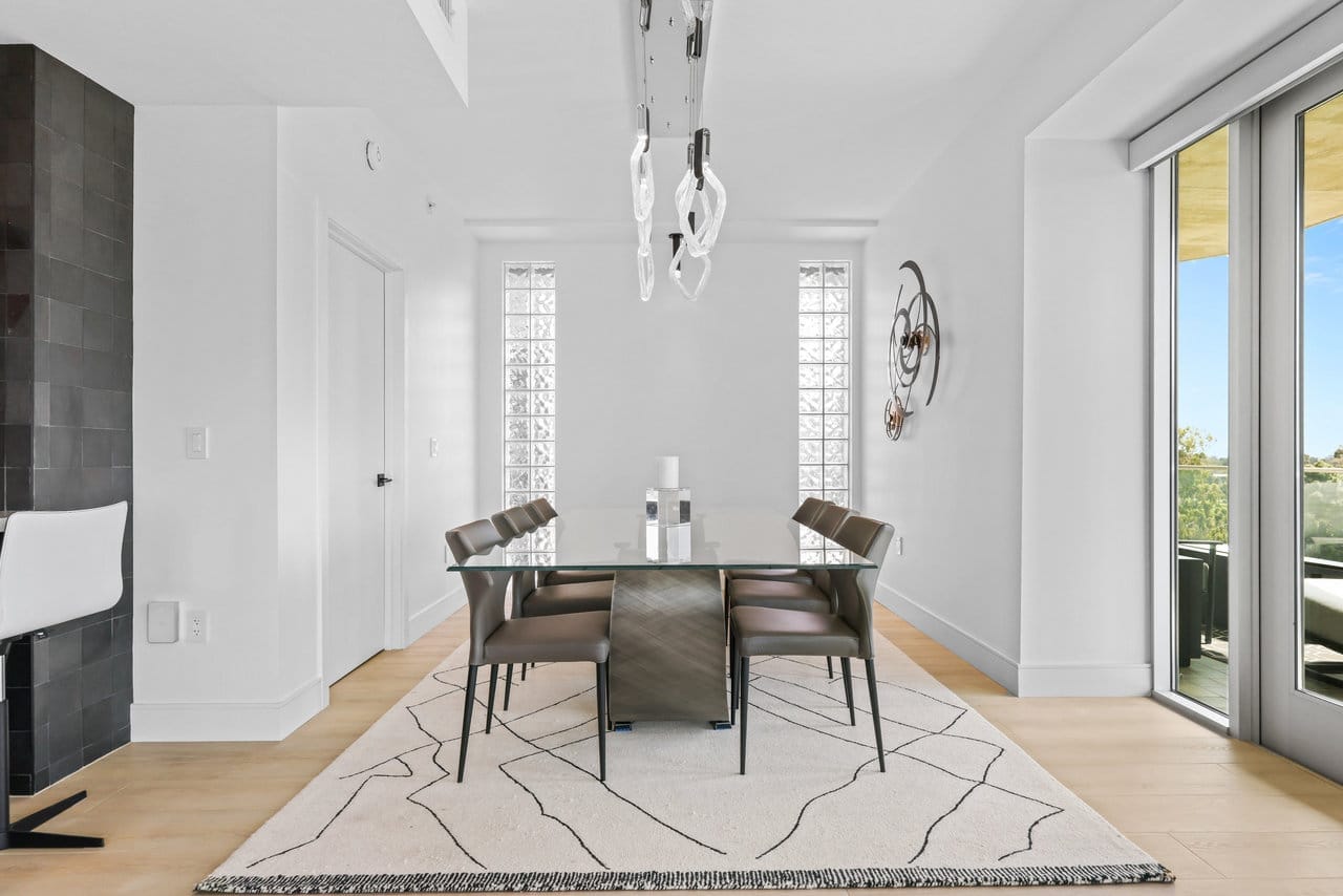 Contemporary dining room with glass table, dark tile accent wall and patterned area rug