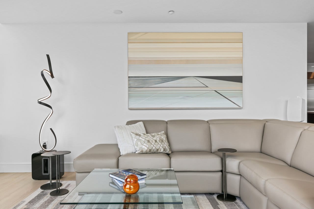 Living room corner with taupe leather sectional, sculptural floor lamp and abstract artwork