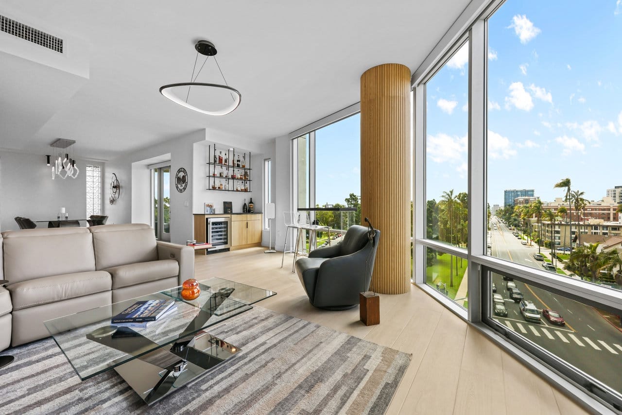 Modern high-rise living room with neutral sectional and floor-to-ceiling windows overlooking palm trees
