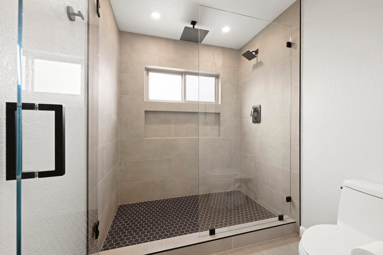 Glass walk-in shower with gray tile, rain head, and hexagon mosaic floor