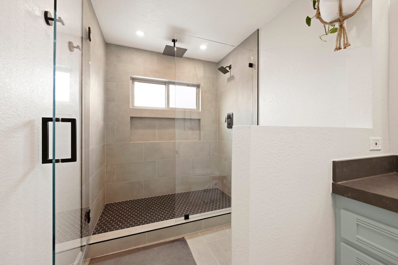 walk-in glass shower with taupe large-format tile and penny-tile floor