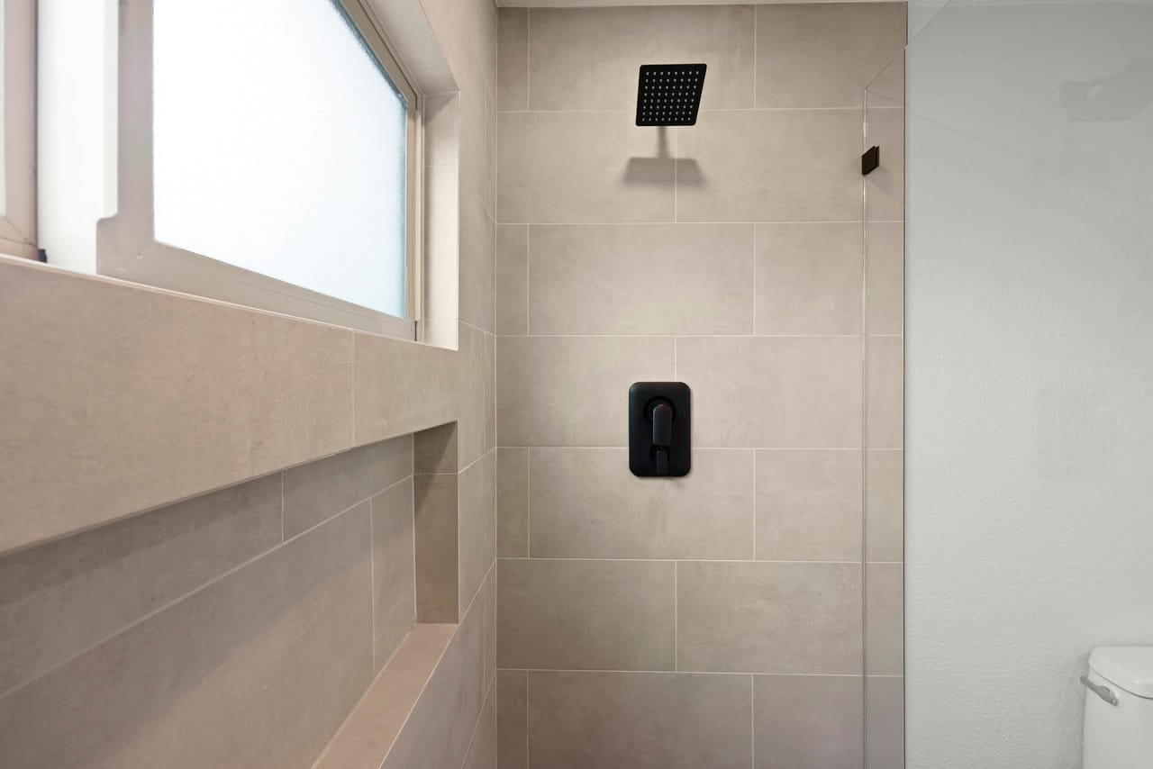 tiled shower wall with matte black rainfall head and recessed niche