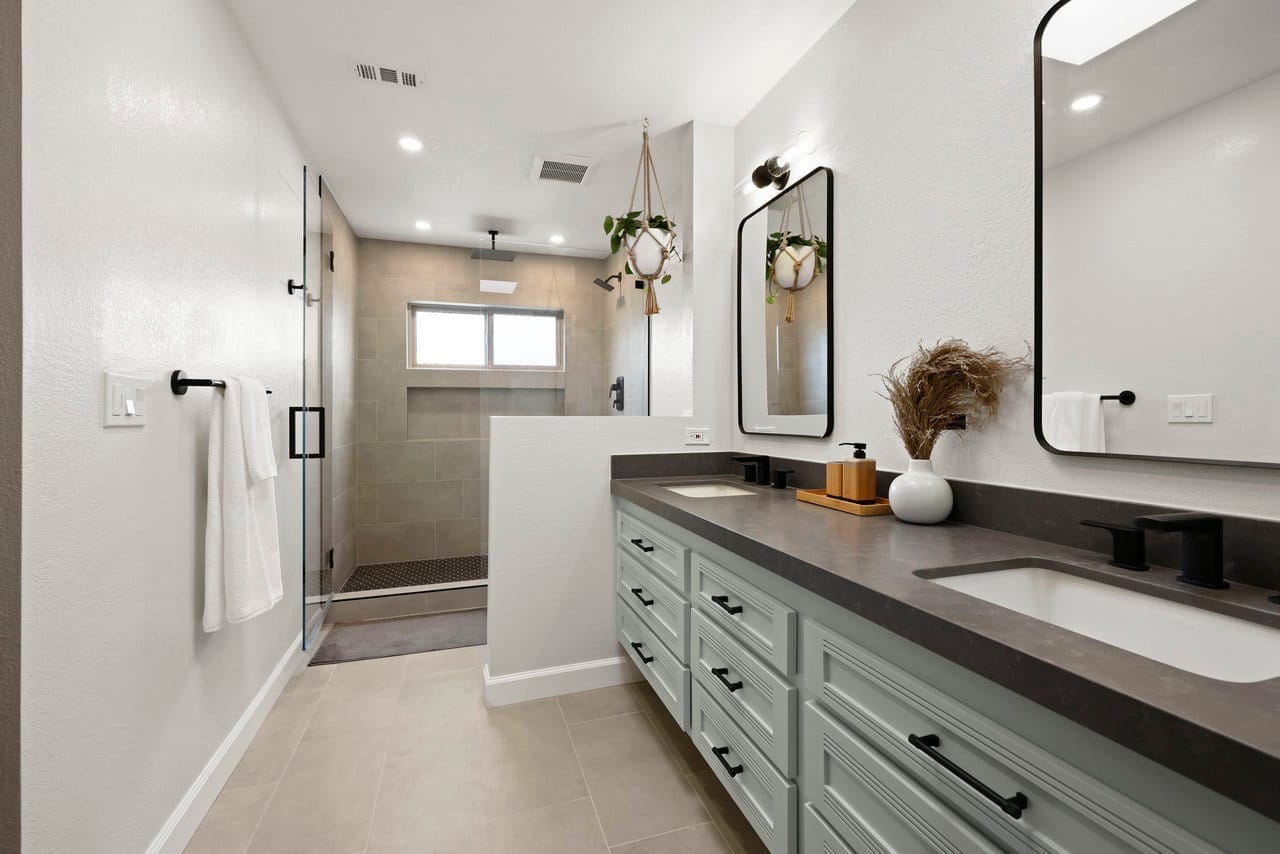 primary bathroom with sage double vanity, dark quartz top and glass shower