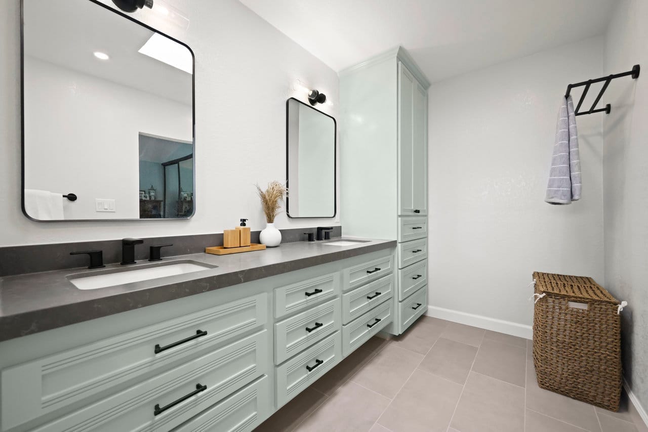 Double-vanity bathroom with sage cabinets, gray quartz top, and black mirrors