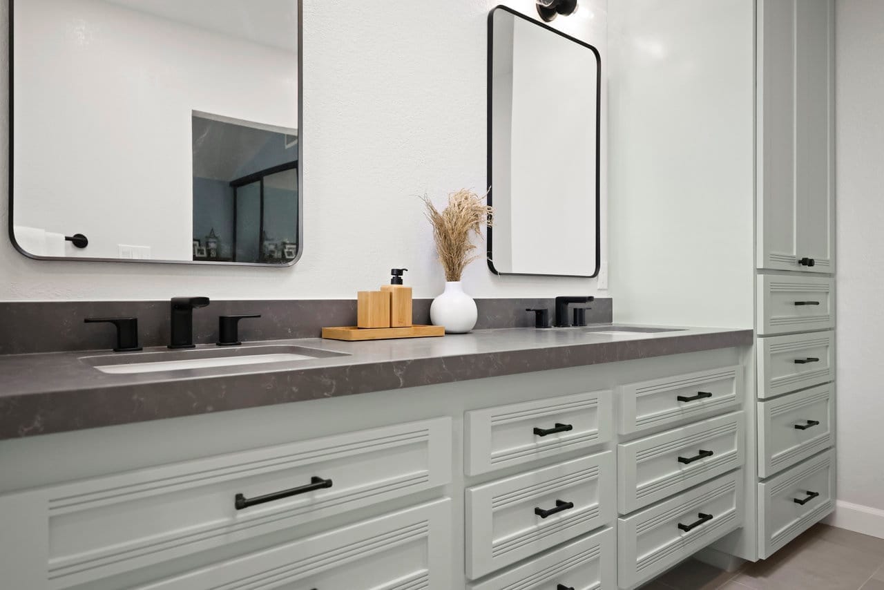 Sage green dual vanity with veined gray countertop and black framed mirrors