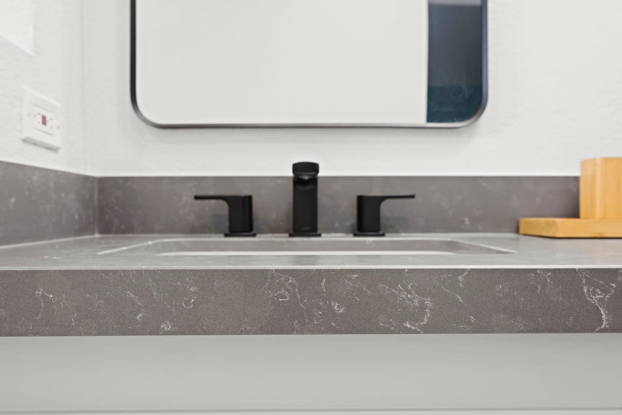 Close view of veined gray quartz counter with black widespread faucet and rectangular sink
