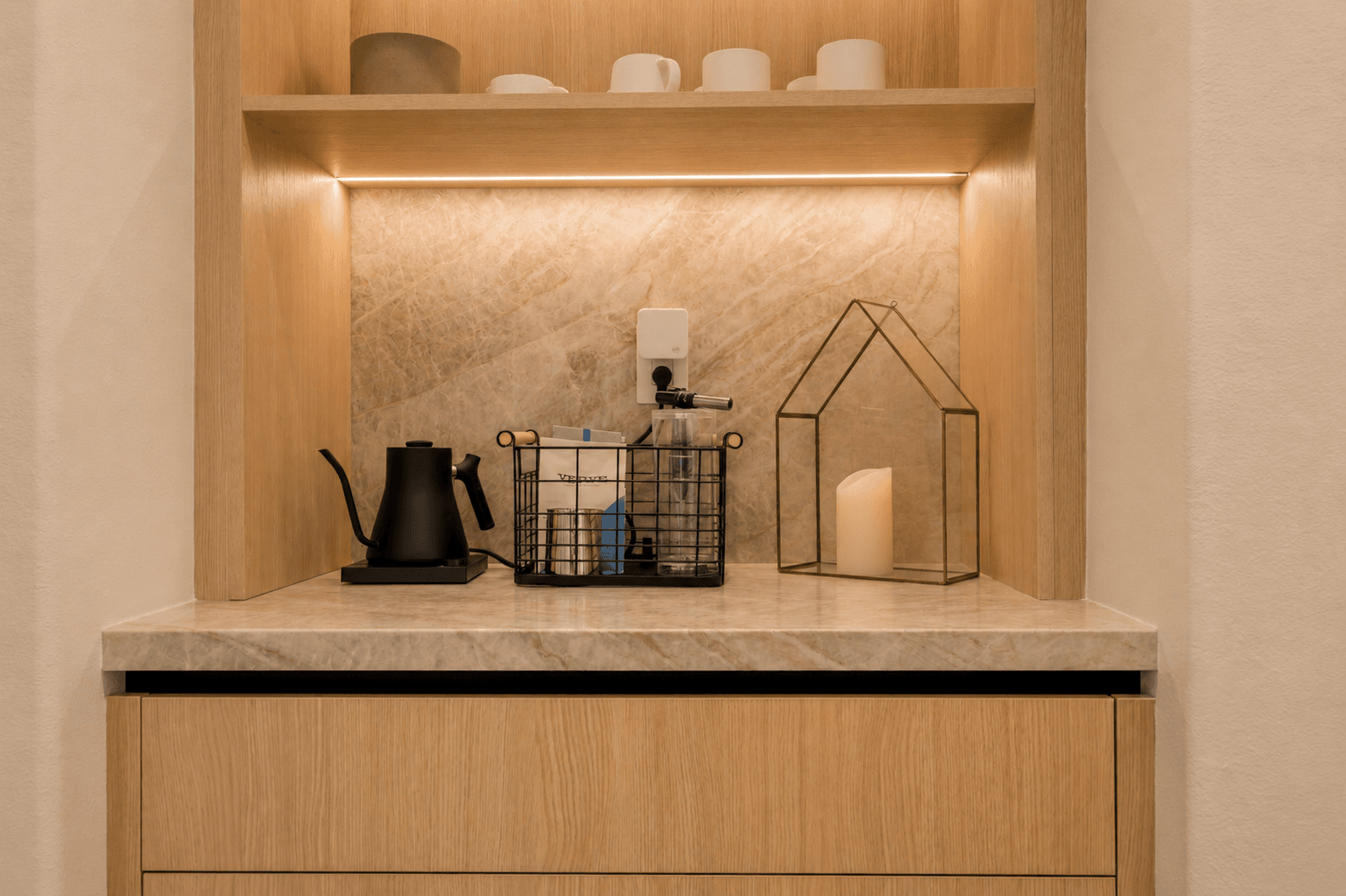 Coffee nook with marble counter, oak cabinetry and warm shelf lighting