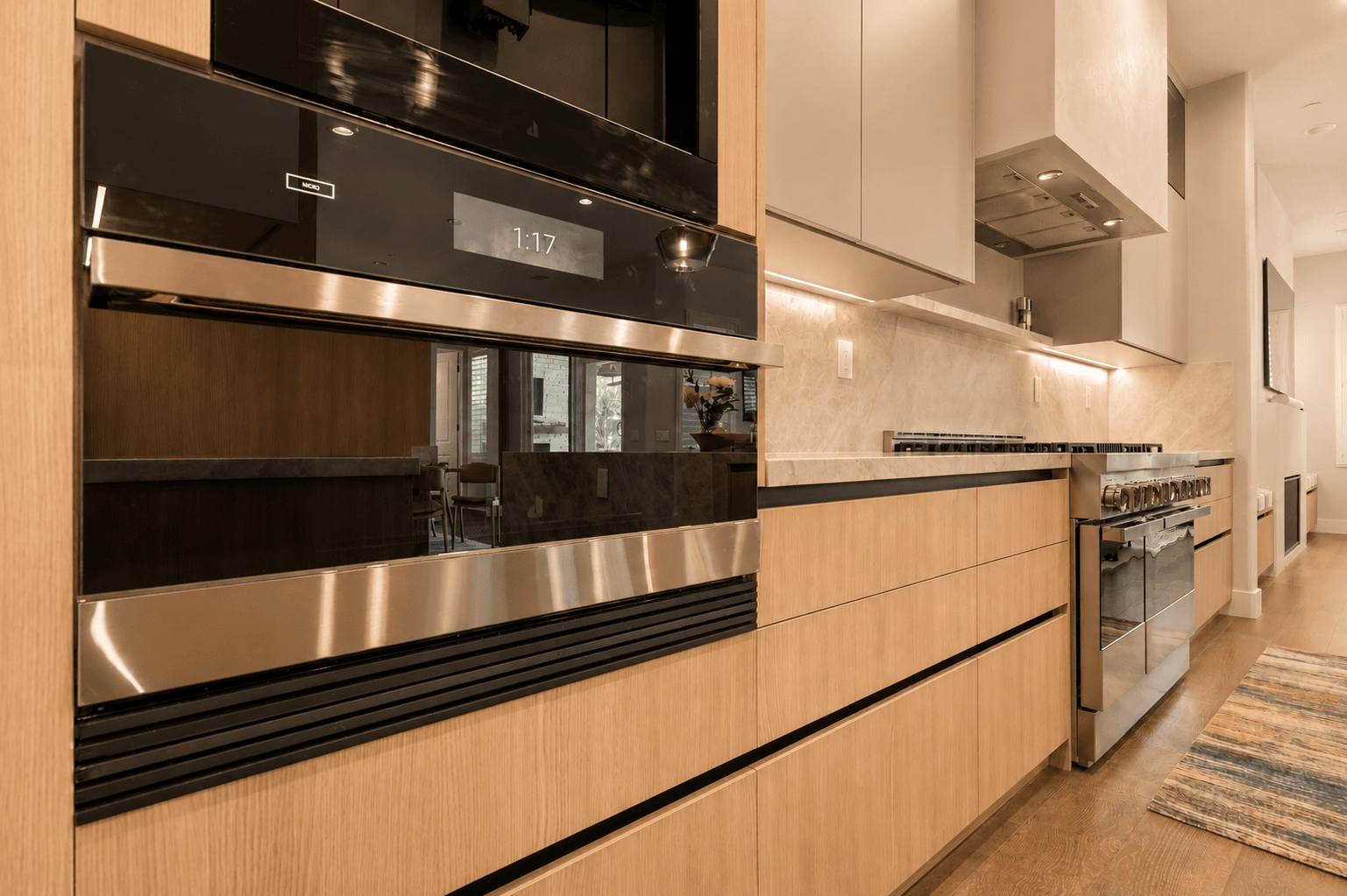 Modern kitchen with light oak cabinetry, black wall ovens and stainless range
