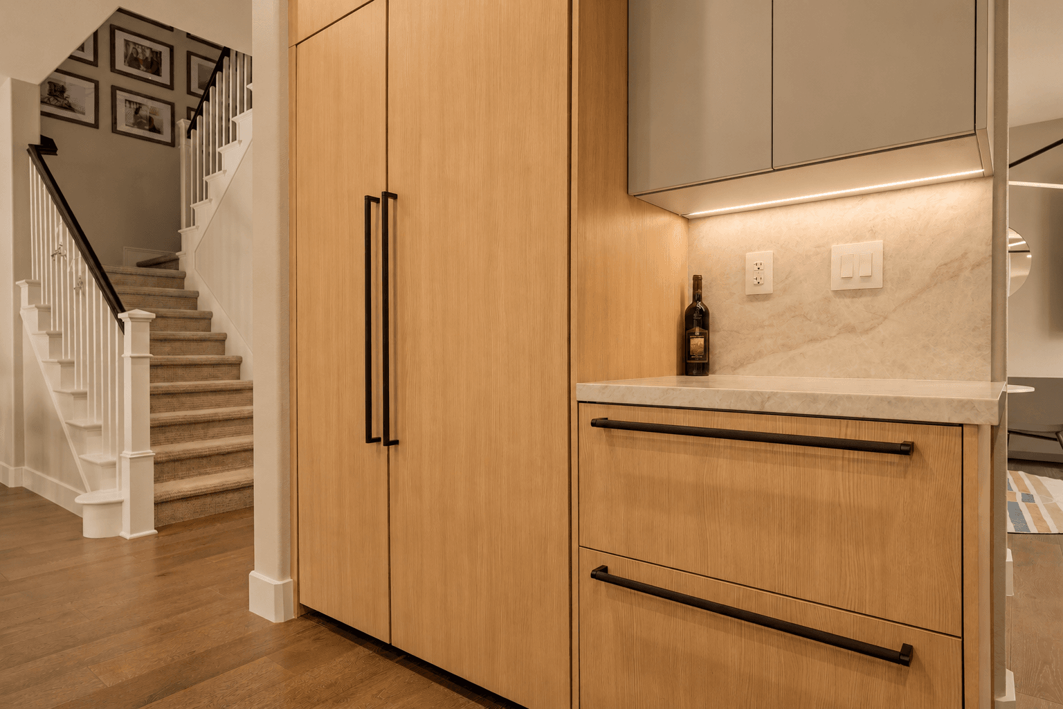 Oak panel-front refrigerator beside staircase with carpeted treads and hardwood floor