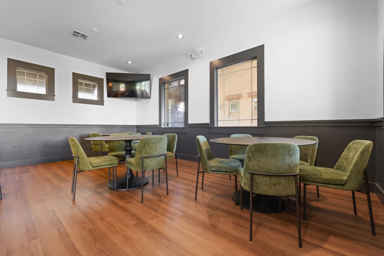 Restaurant dining area with round tables, olive velvet chairs and warm wood flooring