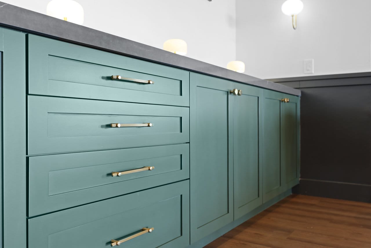 shaker base cabinets in muted teal with brass pulls and dark stone countertop