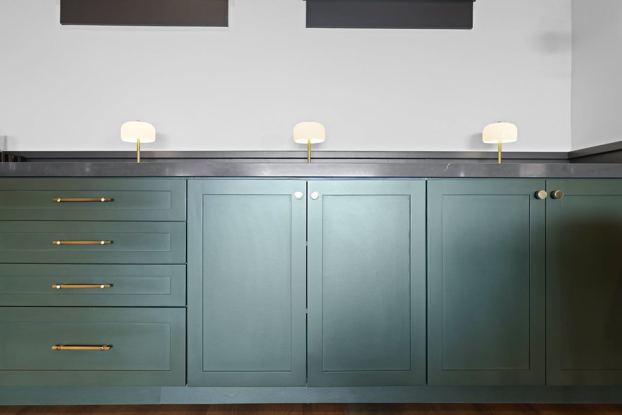 sage green shaker cabinetry with brass hardware below a dark concrete counter