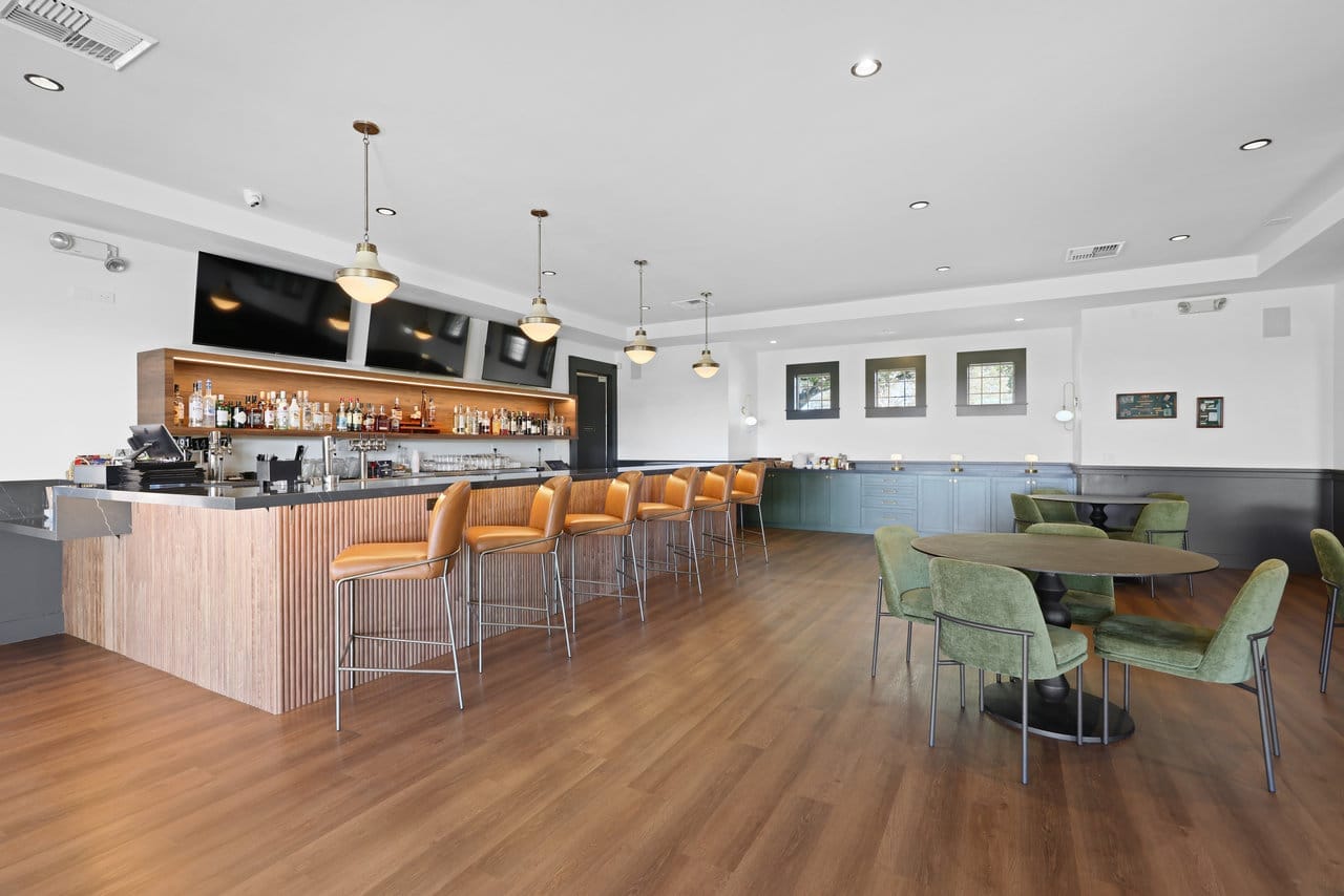 open lounge bar with wood-slat counter, leather stools, and green velvet seating