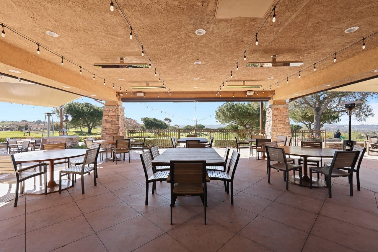 covered outdoor patio with bistro lighting, wood tables, and hillside golf course views