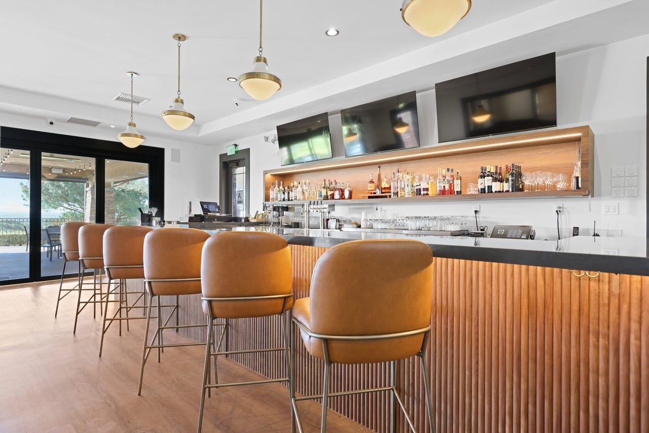 Long bar lined with caramel leather stools, fluted wood front and pendant lighting