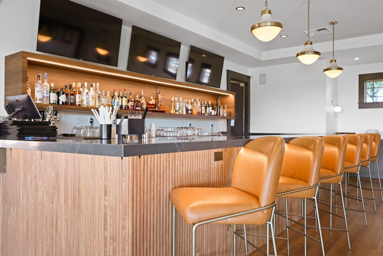 Hospitality bar with wood fluted base, stocked liquor shelves and tan leather barstools