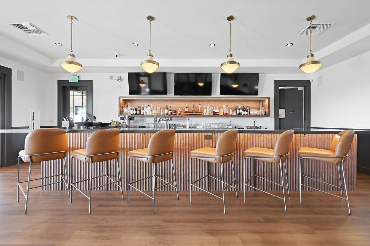 Six caramel leather barstools at a fluted wood bar beneath schoolhouse pendant lights