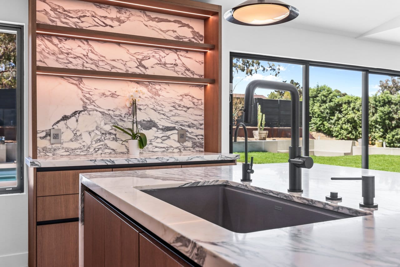 Kitchen island detail with veined marble counter, undermount sink and matte black faucet