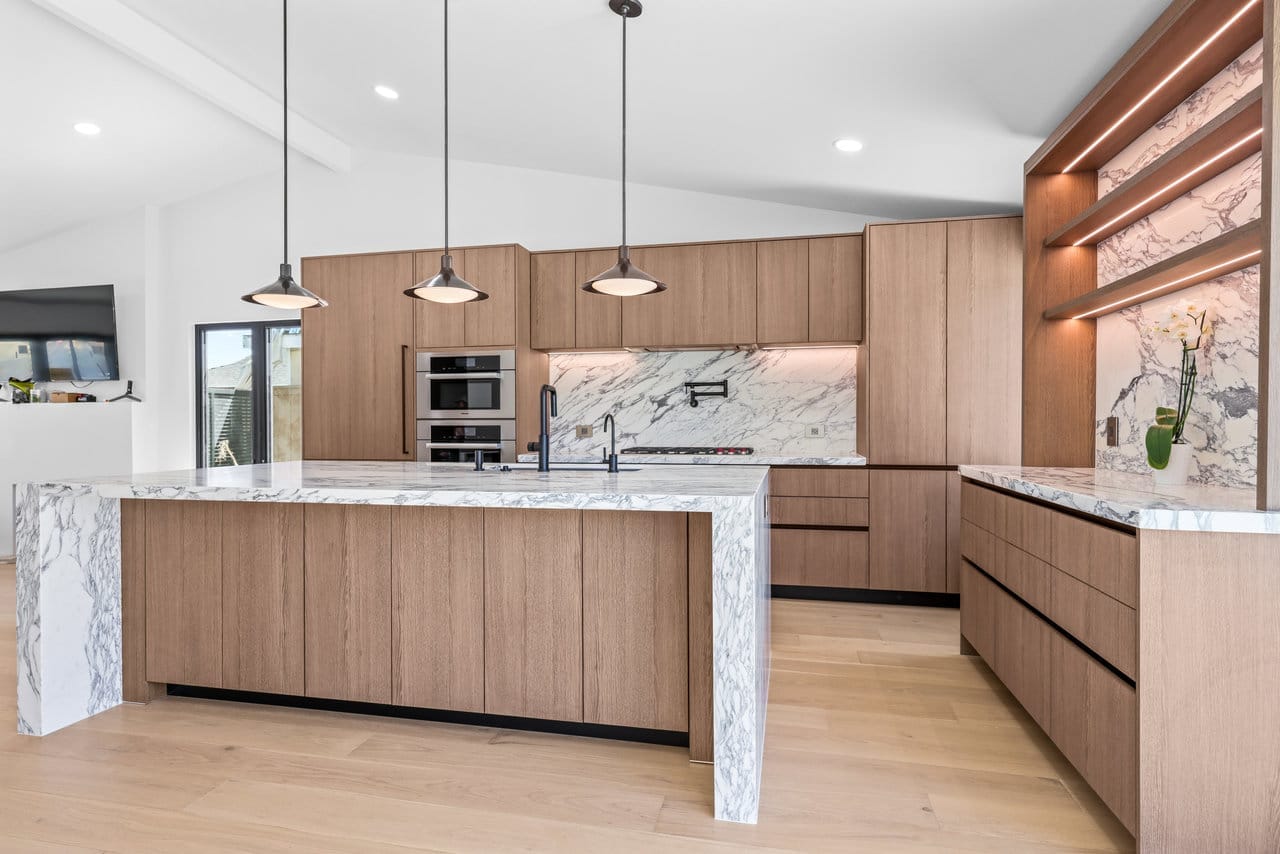 Spacious contemporary kitchen with oak cabinets, marble island and warm pendant lighting