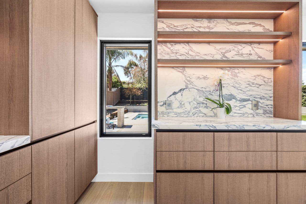 Butler pantry with wood cabinetry, marble backsplash, floating shelves and poolside window