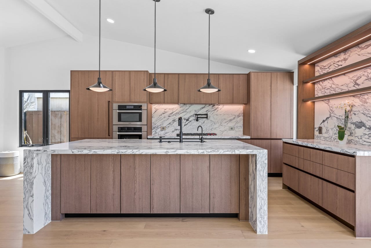 Wood-cabinet kitchen with two marble islands, pot filler, and vaulted ceiling beams