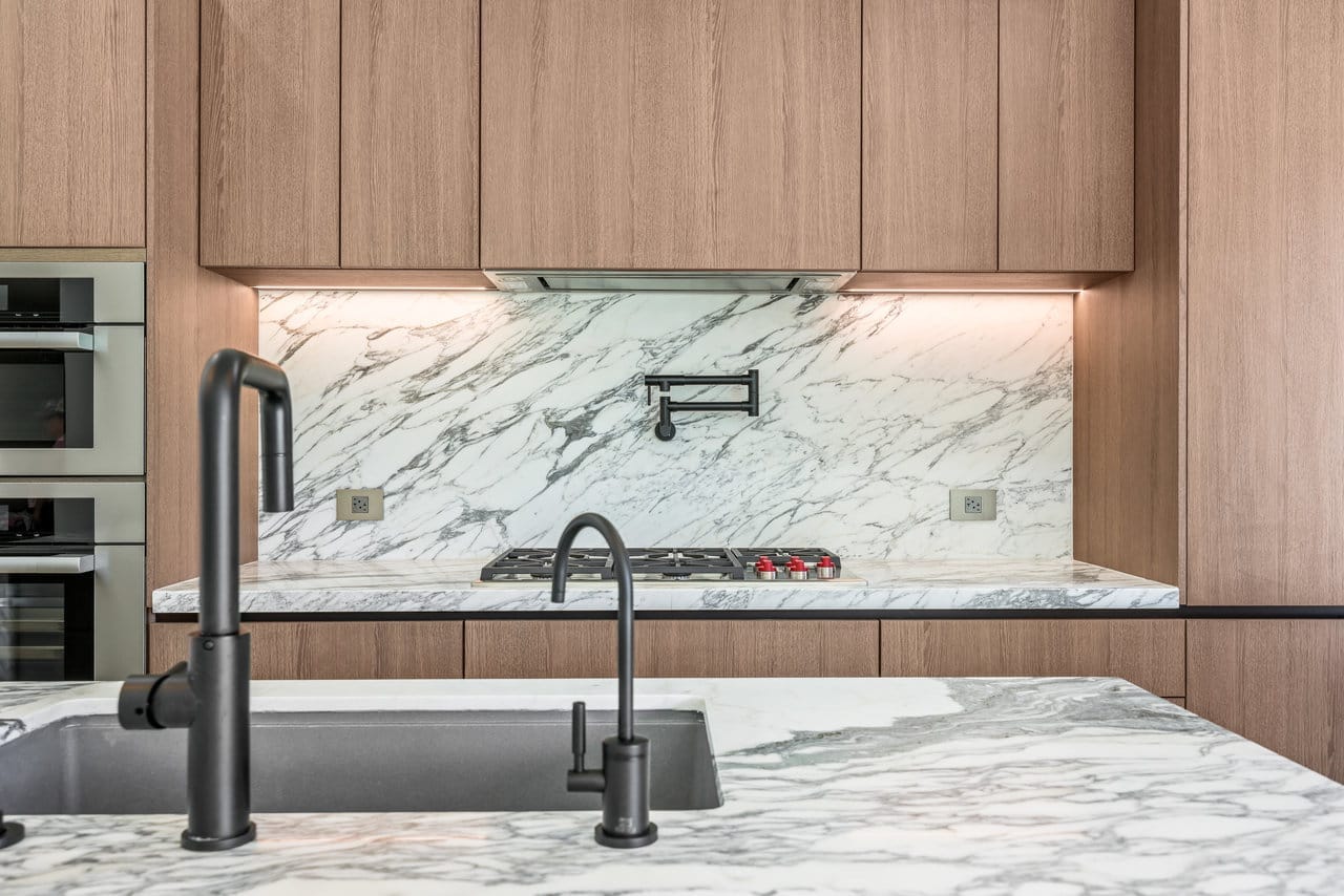 Kitchen close-up with black faucets, gas cooktop, and bookmatched marble backsplash