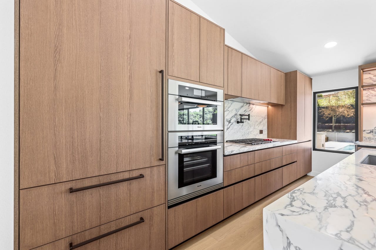 Sleek kitchen wall of oak cabinets with stainless wall oven and marble waterfall counter