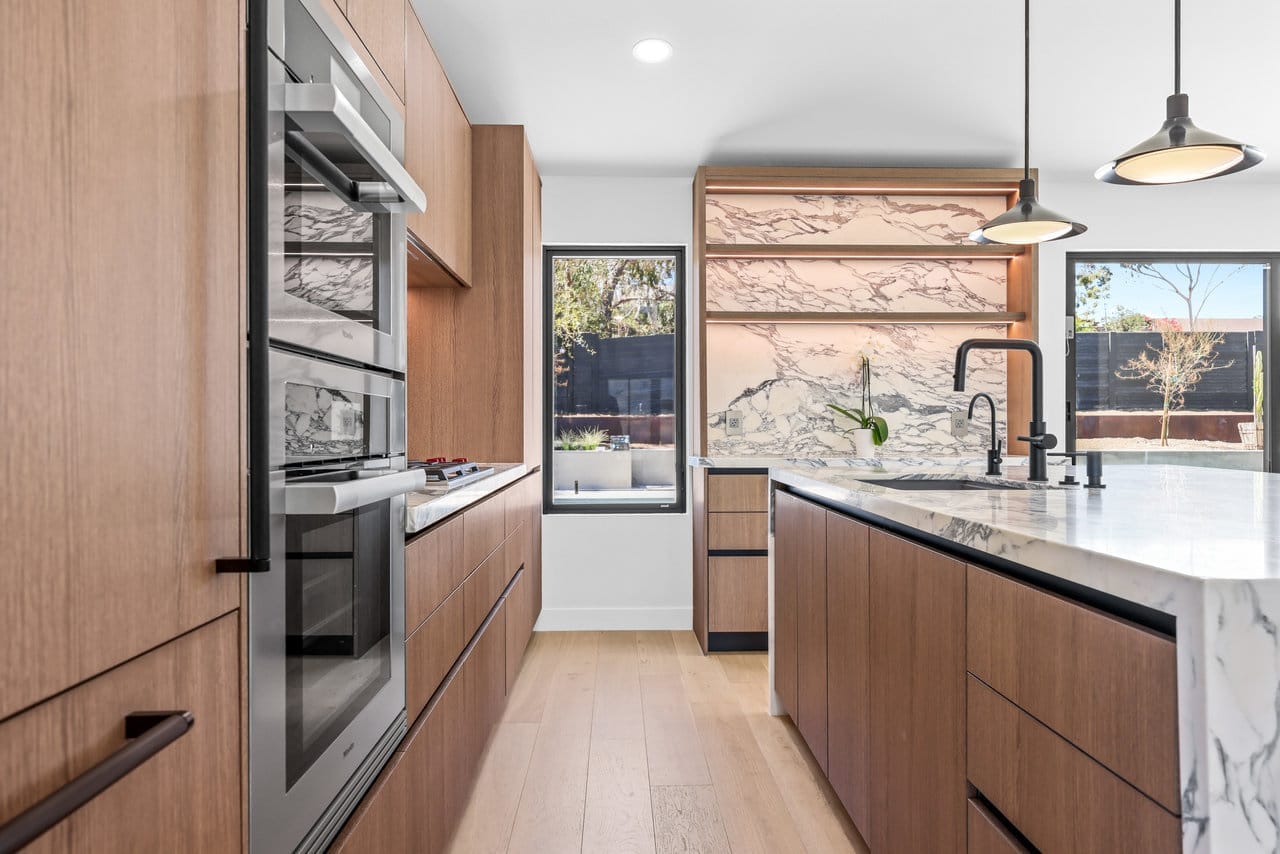 Galley kitchen with wood cabinets, stainless ovens, marble island, and garden window