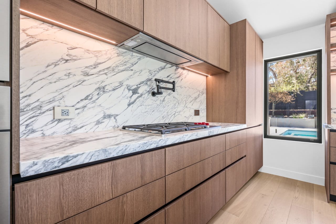 Wood-cabinet kitchen run with gas cooktop, pot filler, and dramatic marble backsplash