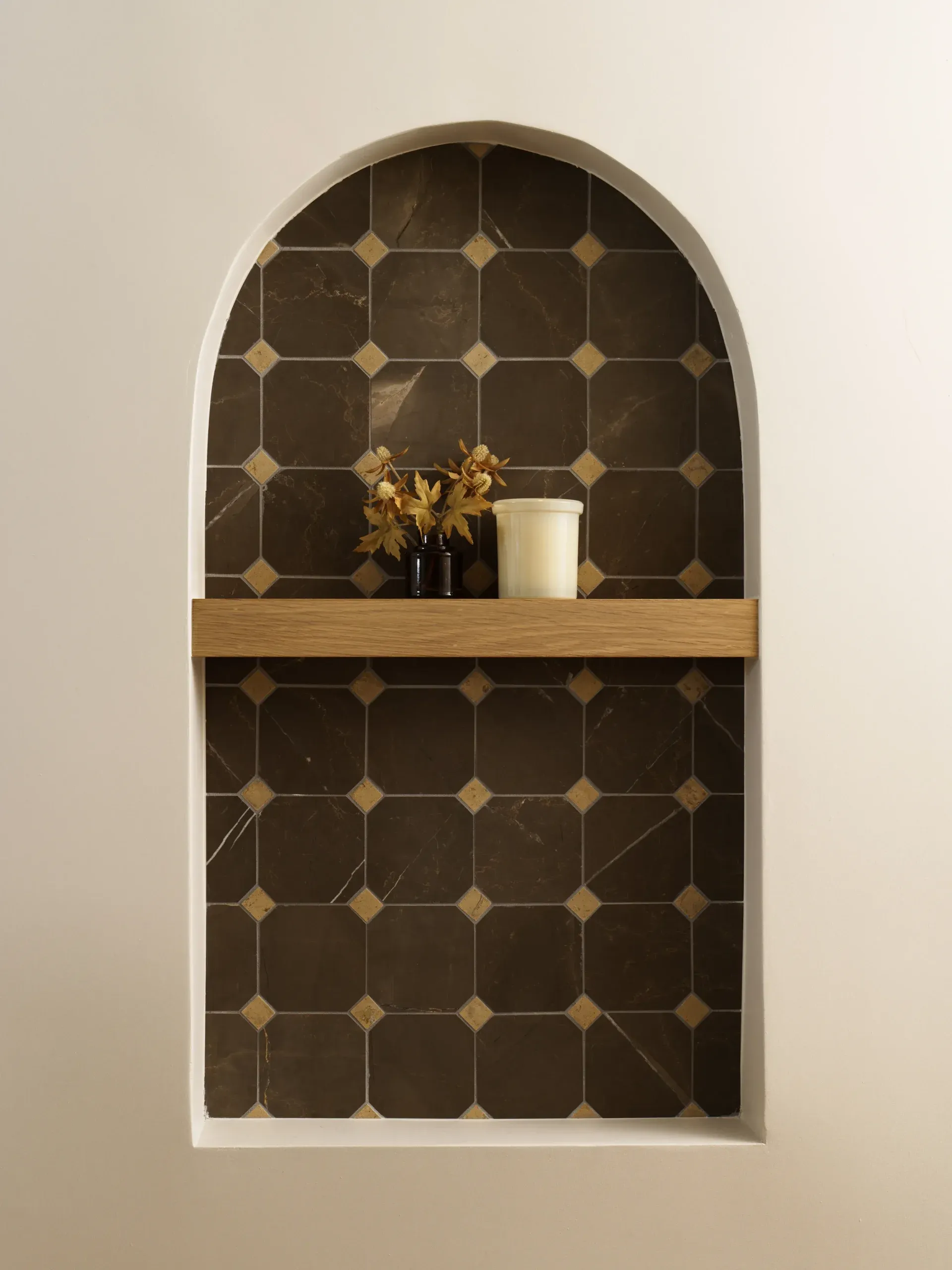 Arched wall niche with dark patterned tile and floating oak display shelf