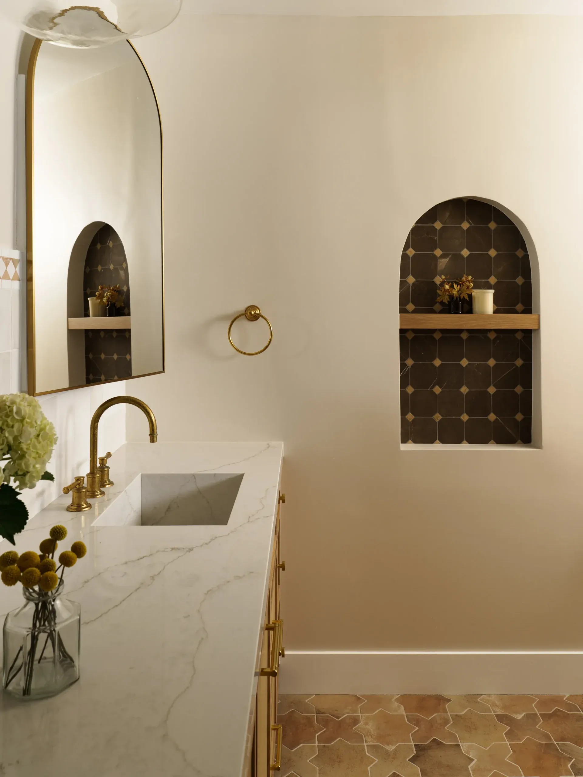 Bathroom vanity with marble counter, brass faucet and arched tiled wall niche