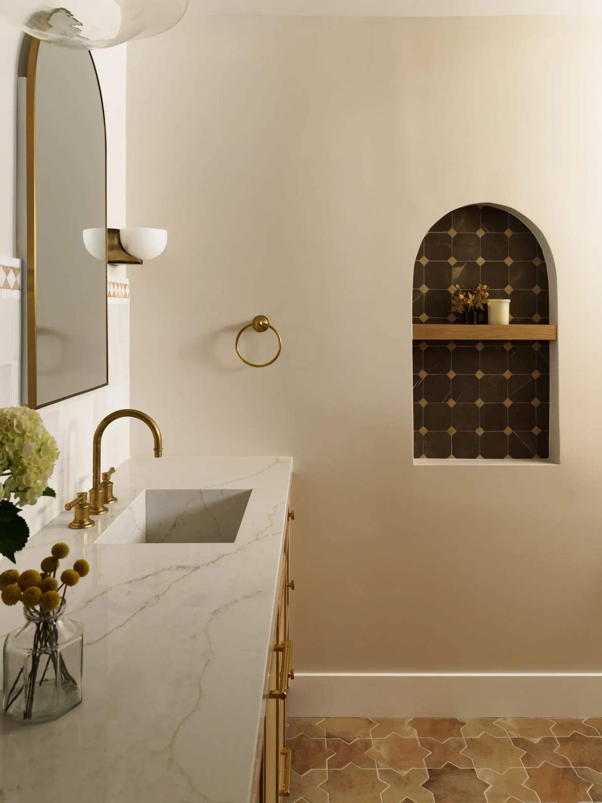 Marble-topped vanity with brass fixtures, arched mirror and tiled niche detail