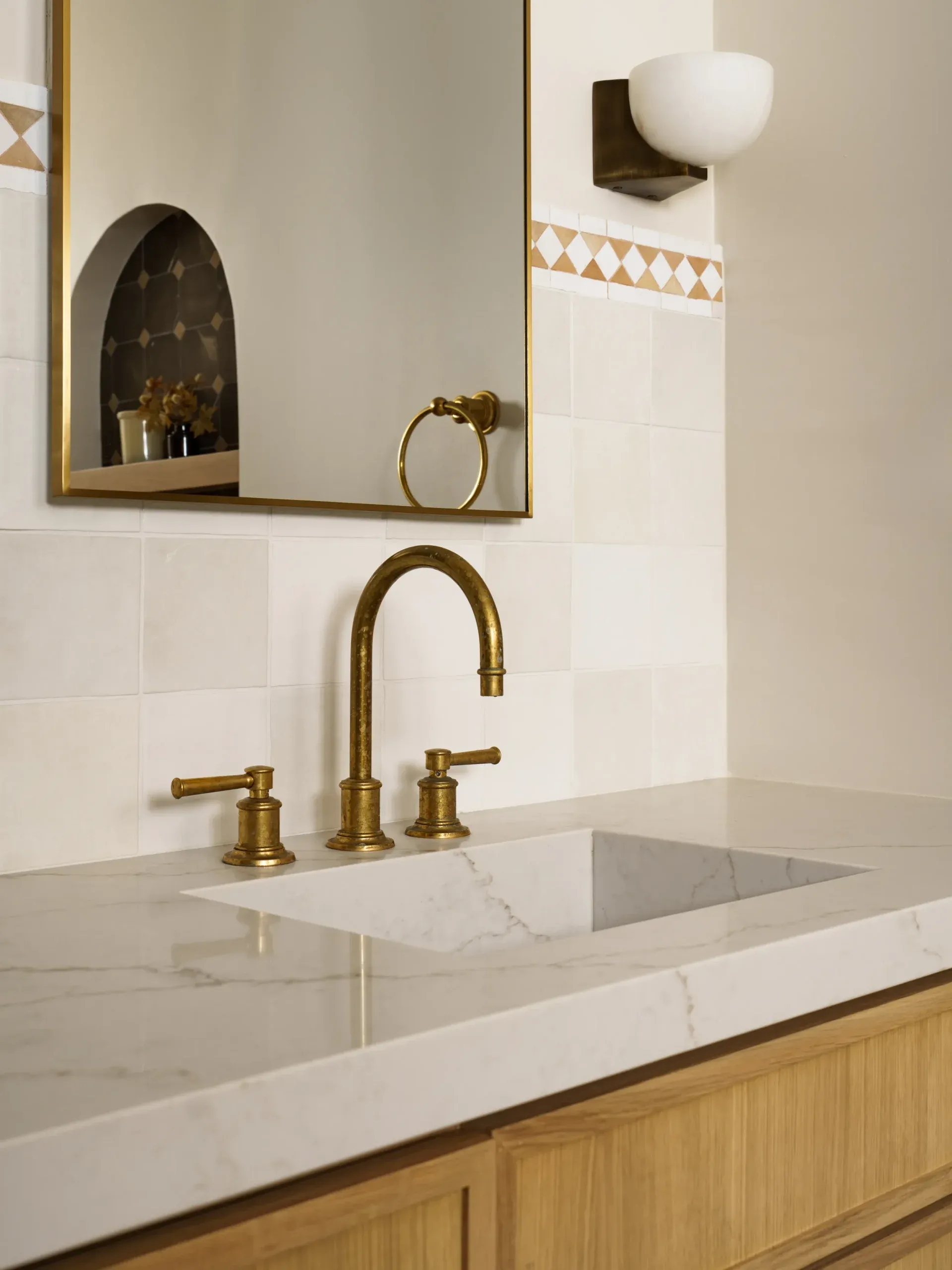 Brass bridge faucet on stone vanity with marble backsplash and arched mirror