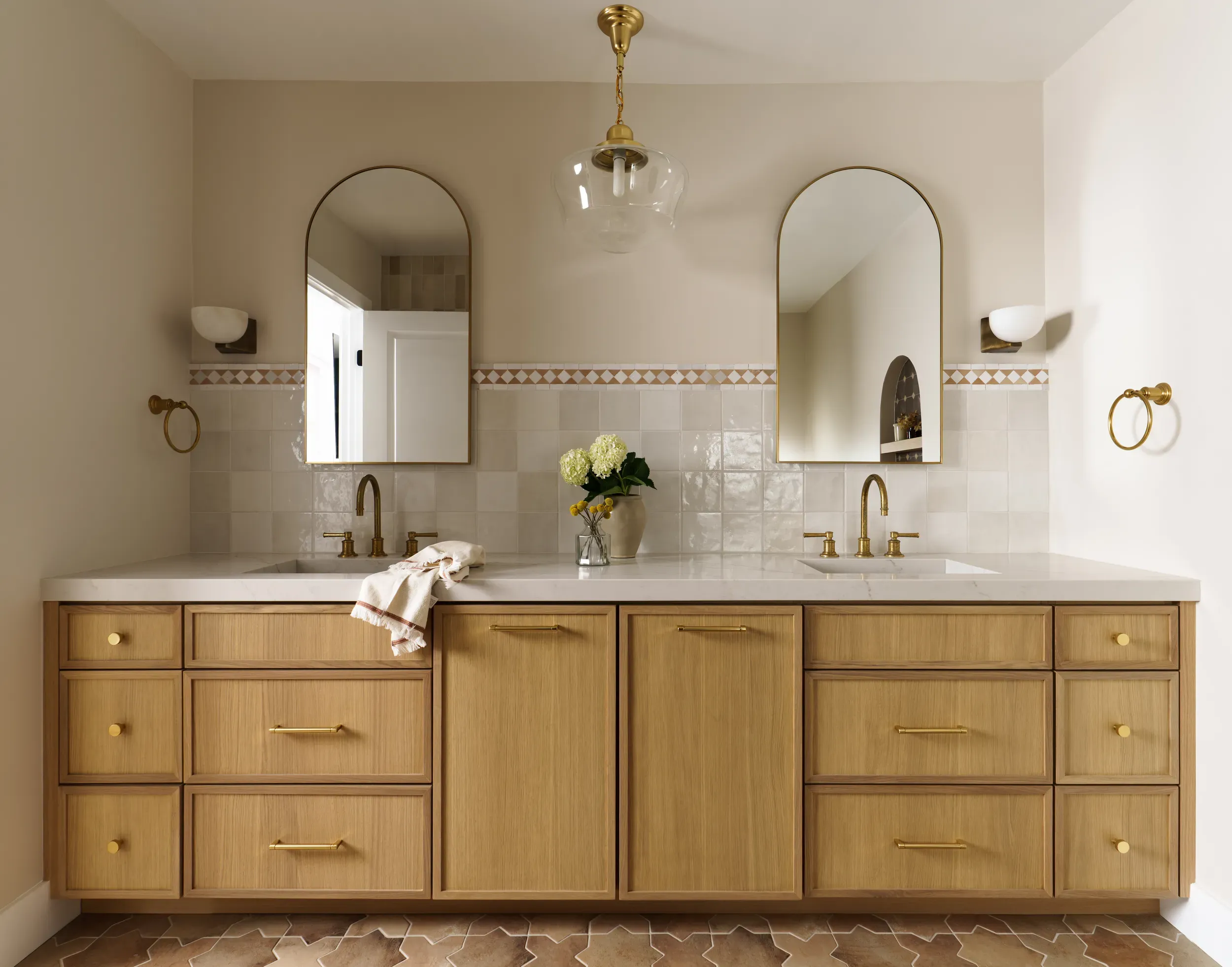 Spanish-style bathroom double vanity with arched mirrors and oak cabinets