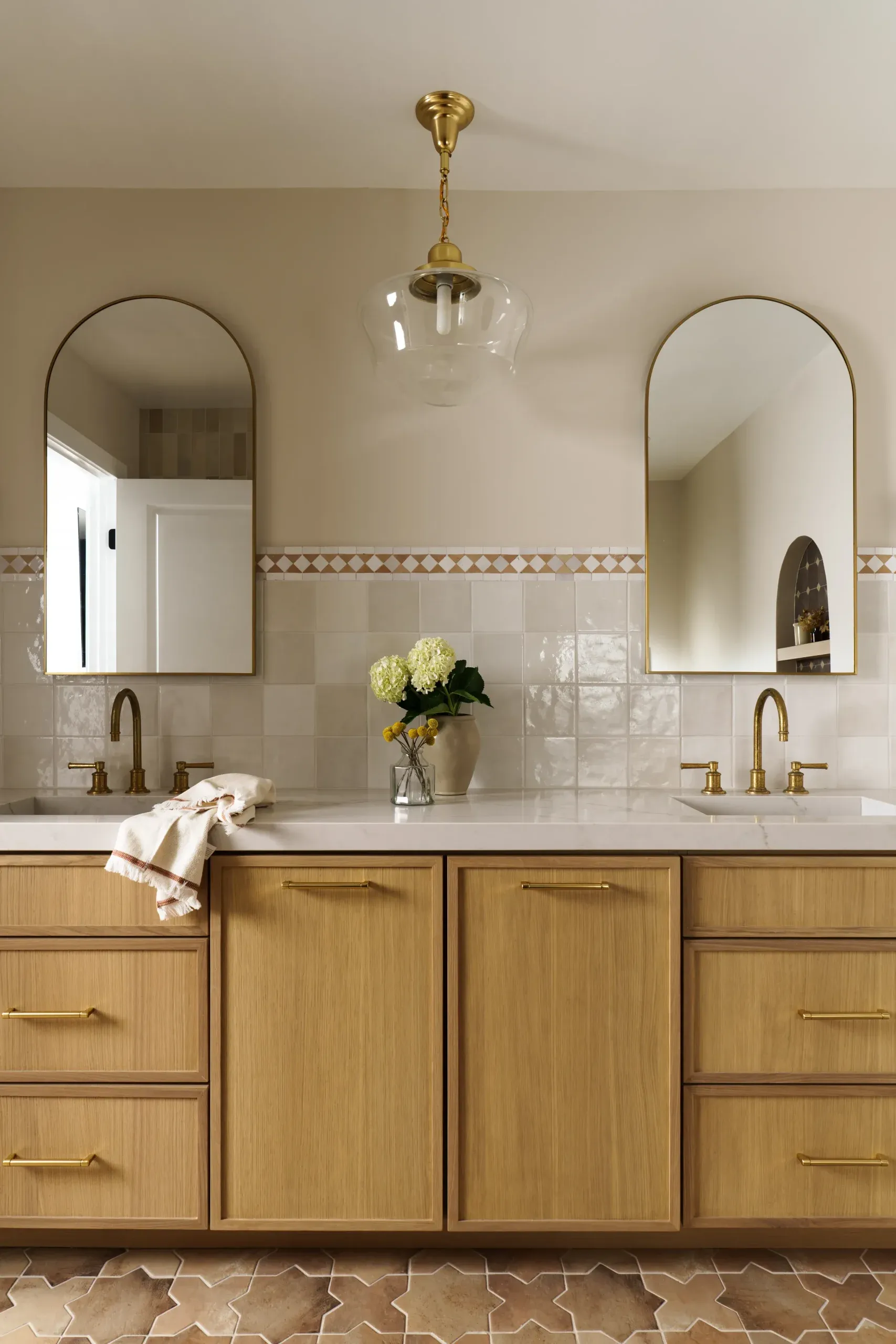 Warm bathroom vanity with arched mirrors, oak cabinets, and terracotta tile floor