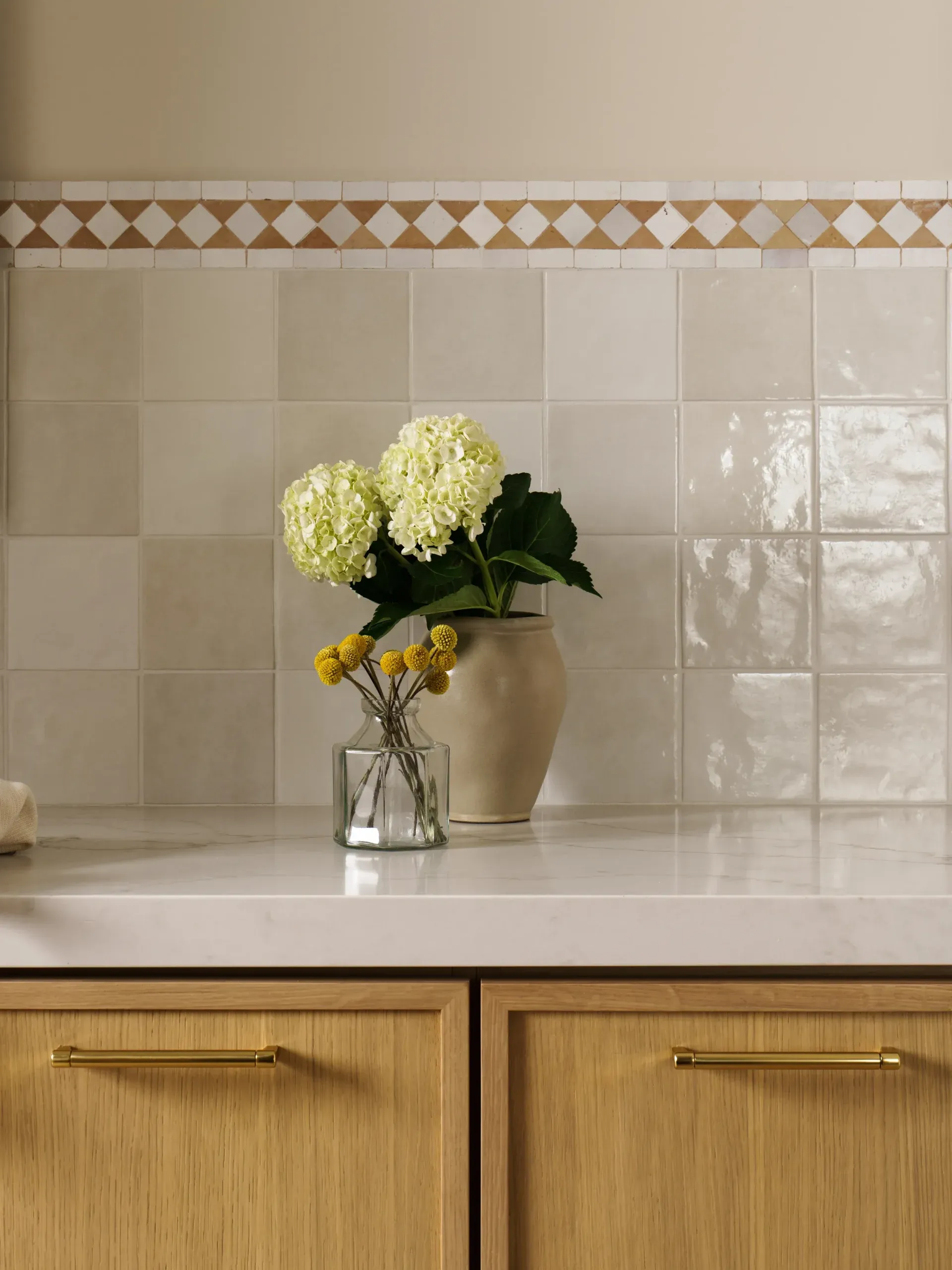 Glossy zellige tile backsplash with quartz counter above oak cabinetry