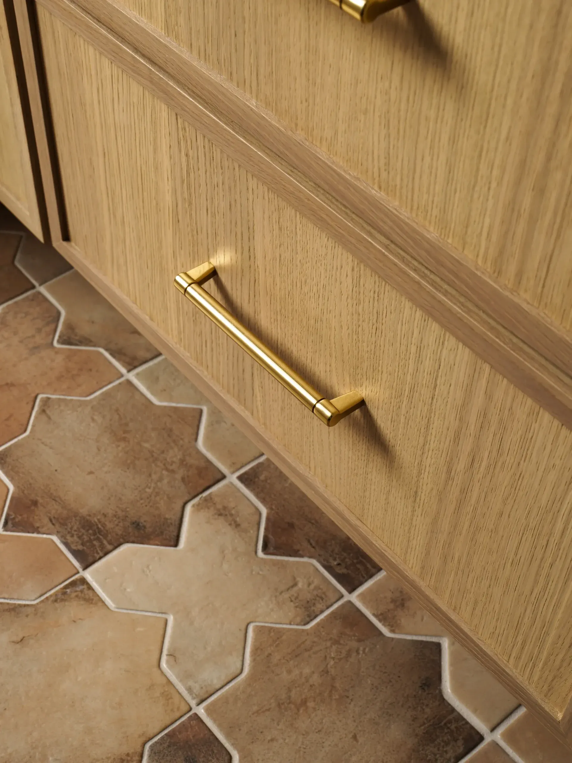 Wood cabinet drawer with brass pull above terracotta star-and-cross tile floor