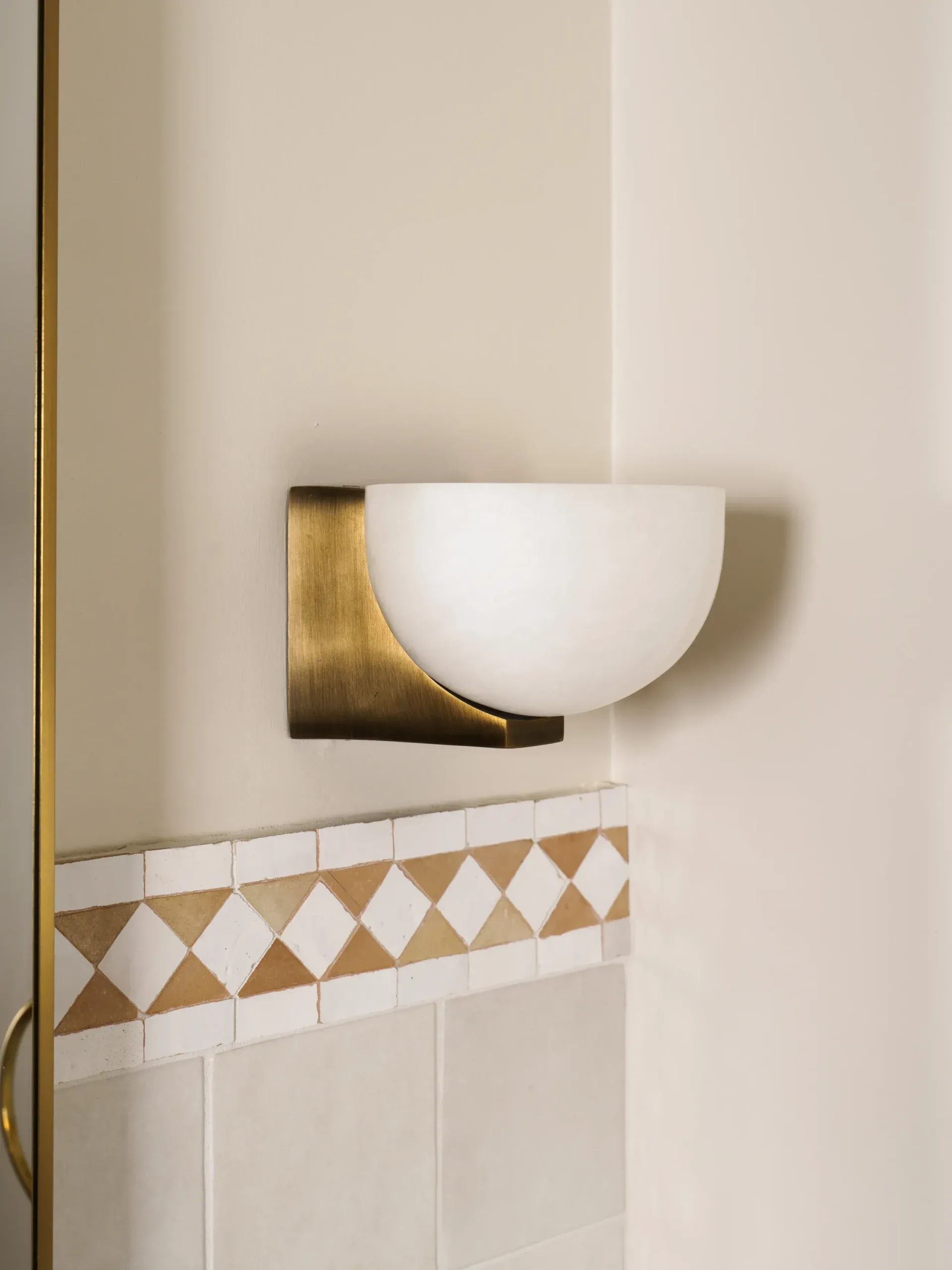 Brass and frosted glass wall sconce above diamond-pattern decorative tile border