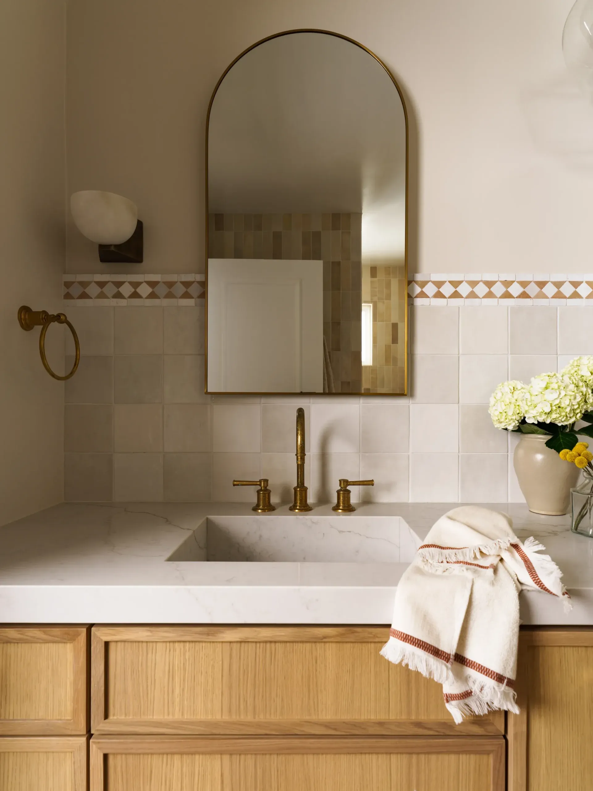 Warm bathroom vanity with arched brass mirror, quilted tile and oak cabinet