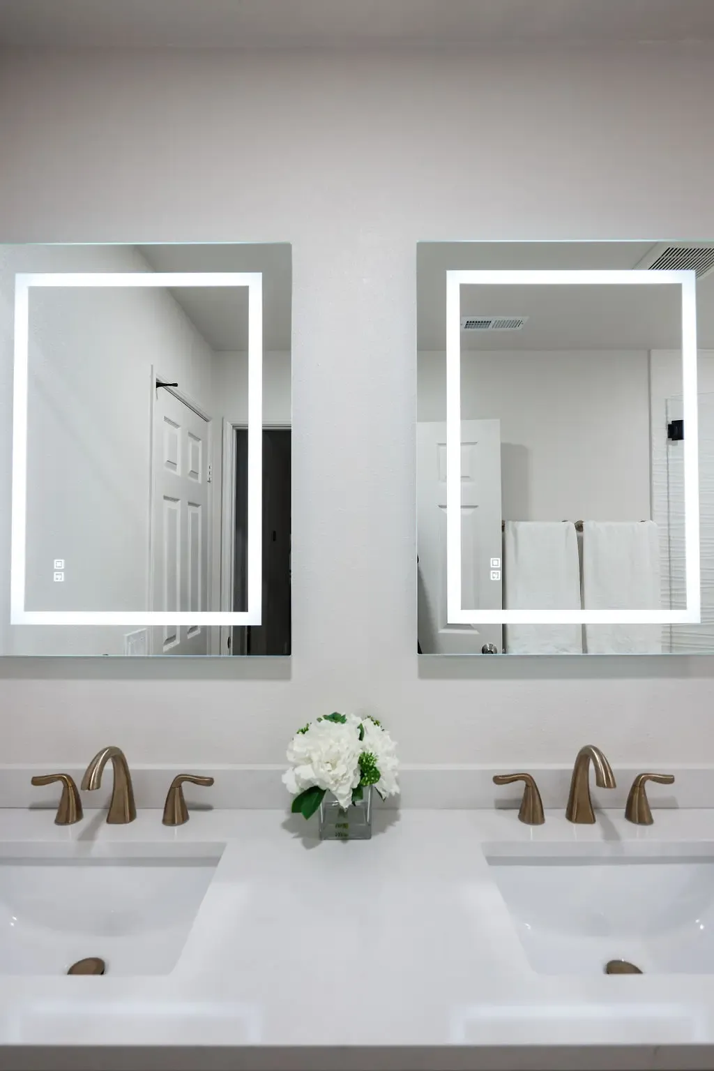 Bathroom vanity with dual LED-lit mirrors, brushed gold faucets and white quartz counter
