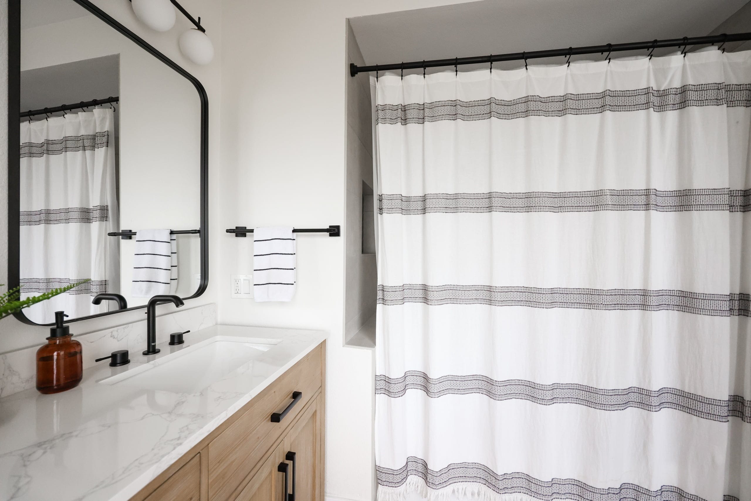 Bathroom vanity with marble top, black fixtures, and gray-striped shower curtain