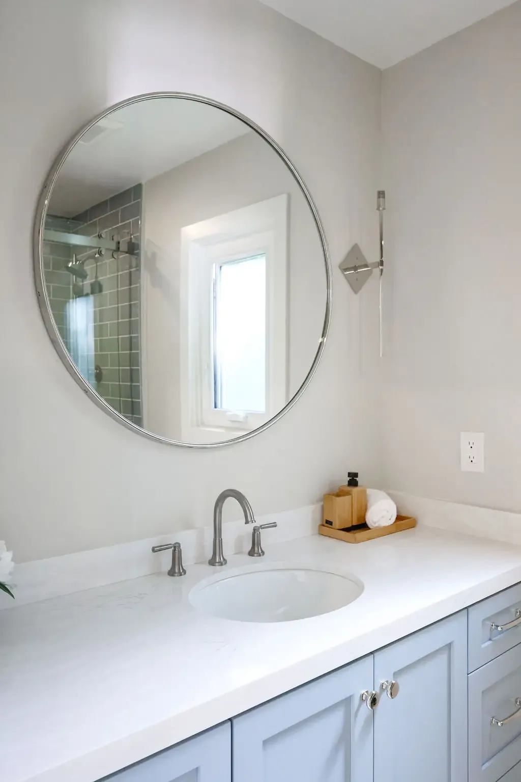 Bathroom vanity with round mirror, gray cabinetry and white quartz top