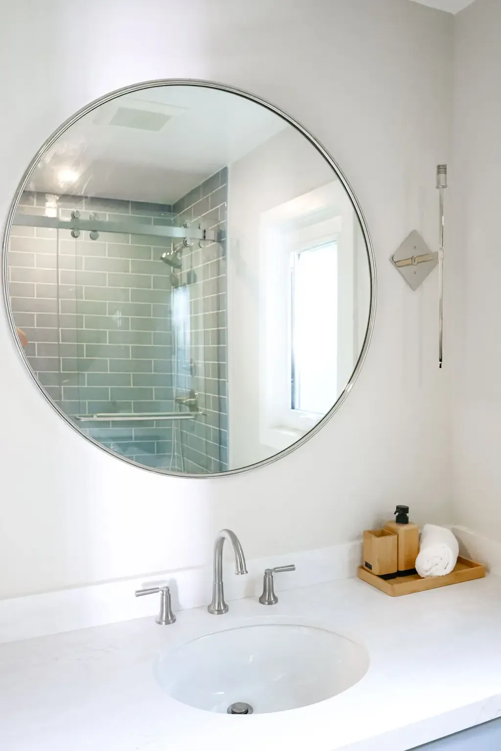 Bathroom vanity with round mirror reflecting blue-tiled glass shower